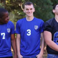 Remilson stands and laughs alongside his brother Zach, a teenage white boy with short black hair, and his brother Alex, a teenage white boy with short black hair. Zach is wearing a Danville soccer jersey similar to Remilson while Alex is wearing a navy blue football jersey.