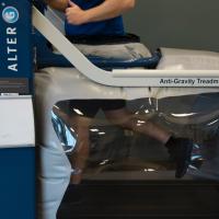 A photo of a person using the anti-gravity treadmill machine—the machine is built as a standard treadmill with gray plastic around the bottom half where the patient runs.