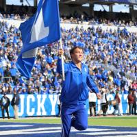 An action shot of Travis running while holding a UK flag at a football game.