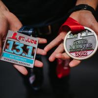 Trent holds out two medals in his hands. On his left hand is a silver medal from a St. Jude 13.1-mile half marathon, and on his right hand is a gold medal from a St. Jude 26.2-mile marathon.