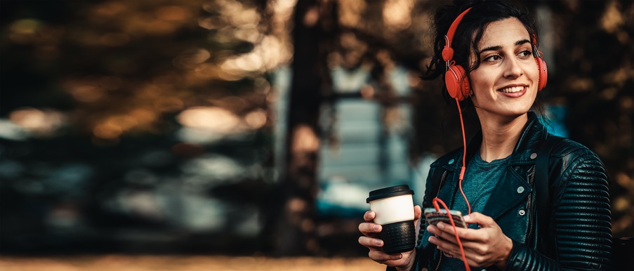 A woman wears red headphones and drinks coffee.